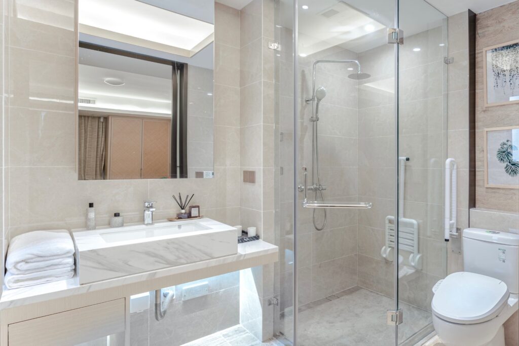 Modern bathroom with laminate flooring, a glass-enclosed shower featuring expert tile installation in Georgia, a wall-mounted toilet, large sink with marble countertop, and neatly folded towels.