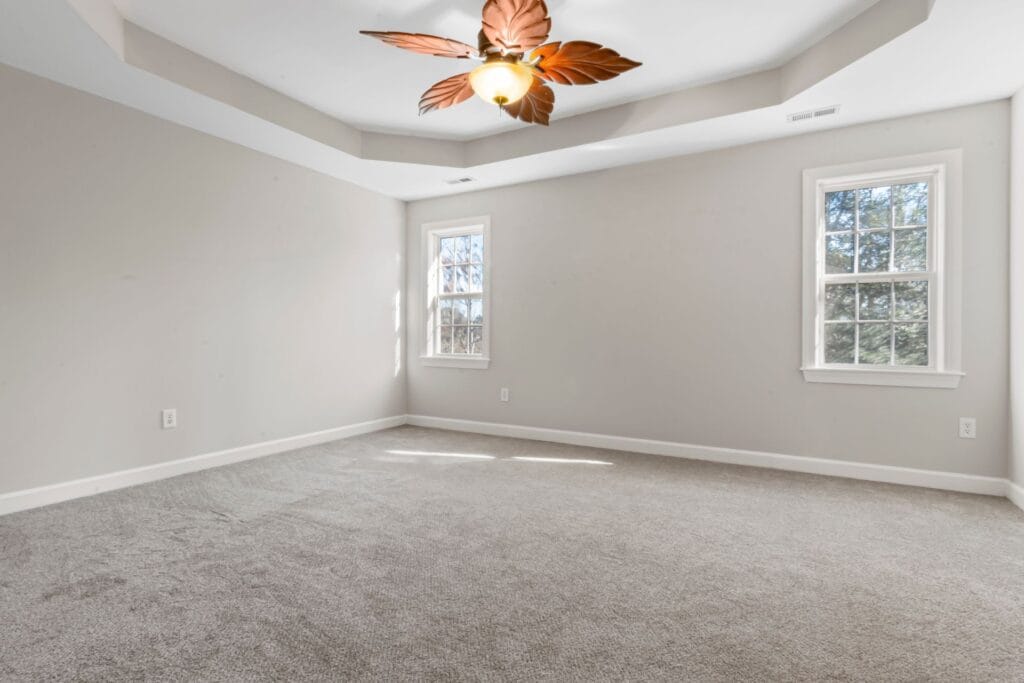 Empty carpeted room with beige walls, two windows, and a ceiling light fixture with leaf-shaped blades&mdash;showcasing professional carpet fitting and installation for a polished finish.