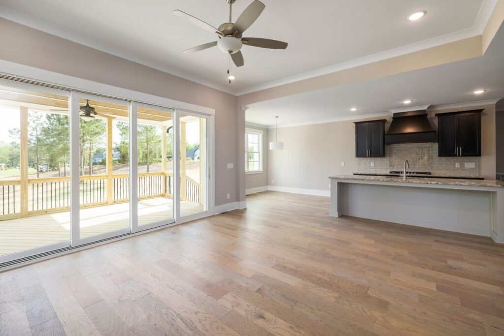 Open-plan living space with light wood floors—perfect for those considering LVP installation cost in Georgia—large sliding glass doors to a covered patio, modern kitchen with dark cabinets, granite counters, and a ceiling fan.