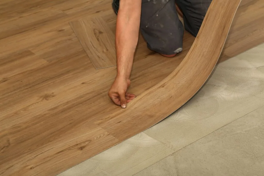 A person completes flooring installation by pressing a luxury vinyl plank into adhesive on the subfloor, creating a seamless wood-look finish, highlighting a key step in understanding LVP installation cost in Georgia.