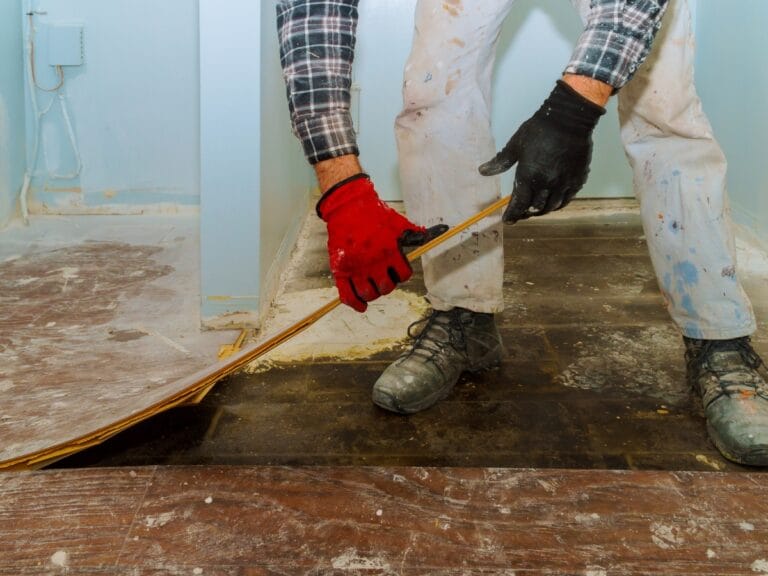 Professional wearing gloves and plaid shirt removing old flooring in a home renovation project, showcasing flooring removal process in Marietta, GA.