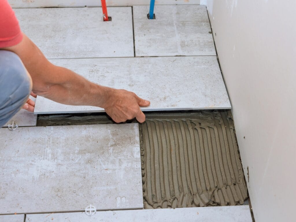 A person installs a floor tile by placing it onto adhesive mortar, aligning it with other tiles in a room under renovation, demonstrating expert flooring repair Marietta homeowners can trust.
