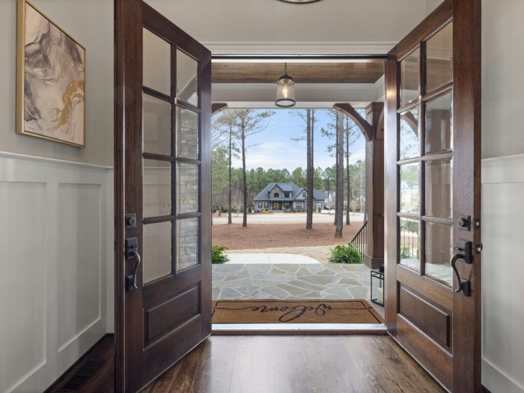 Open double front doors reveal a stone porch, a welcome mat, and a view of a house across a yard with trees and clear sky&mdash;perfect inspiration for Residential Entryway Ideas.