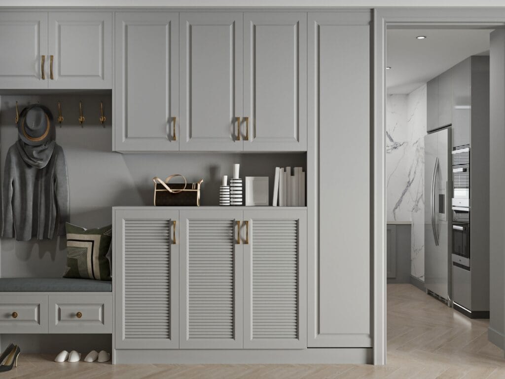 A modern mudroom offers stylish Residential Entryway Ideas with gray built-in cabinets, bench seating, hooks for coats and hats, books, and a view into a kitchen featuring stainless steel appliances.