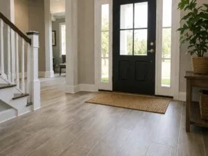 A bright entryway with light wood flooring, a black front door with glass panels, a brown doormat, and potted plants on a wooden table offers stylish Residential Entryway Ideas for welcoming guests.