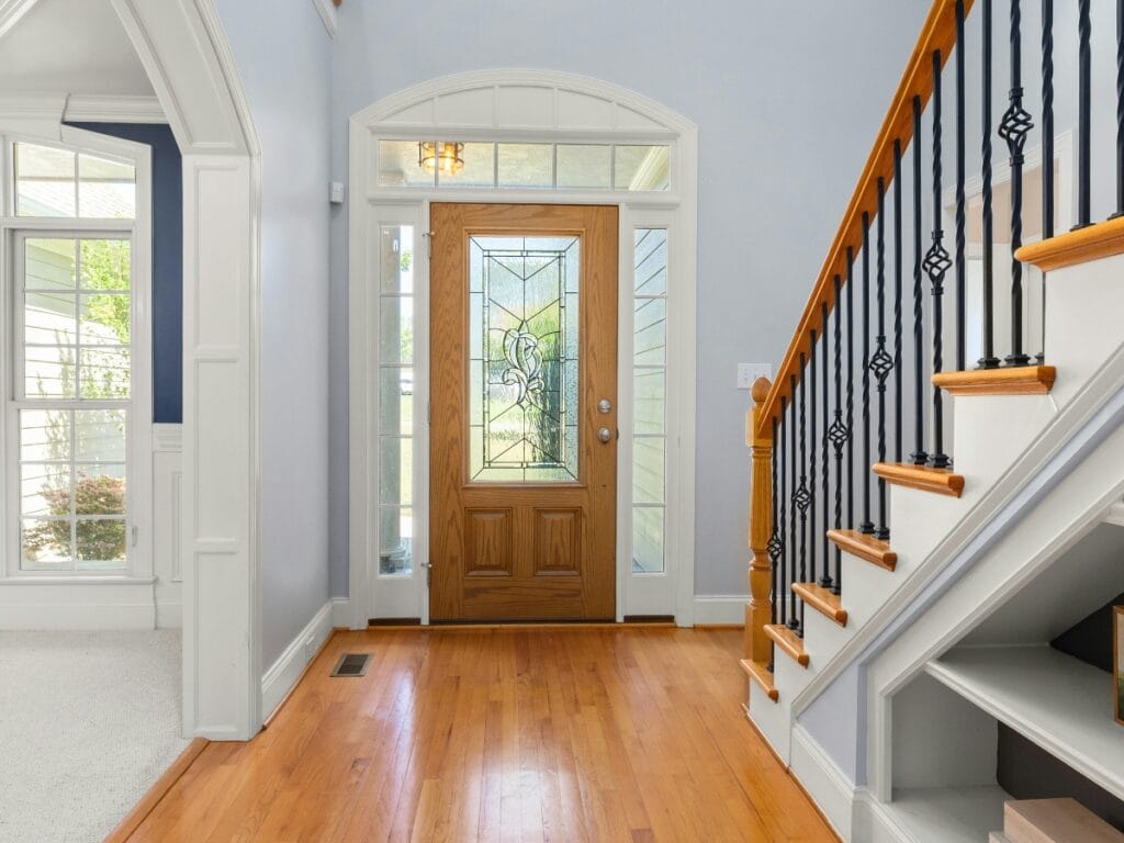 Bright entryway with a wooden front door featuring decorative glass, hardwood floor, white trim, and a staircase with black and wood banister on the right&mdash;perfect inspiration for residential entryway ideas.