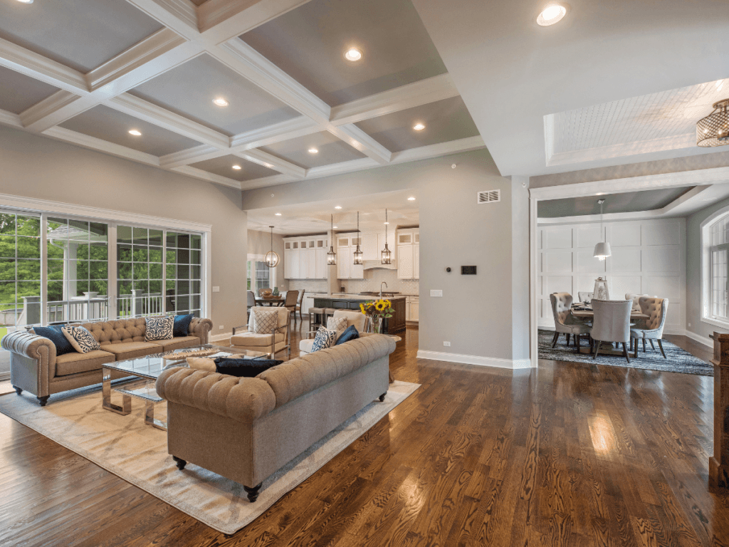 Spacious open-concept living area with hardwood floors, coffered ceiling, neutral d&eacute;cor, large windows, and view of kitchen and dining room&mdash;meticulously maintained with recent flooring repair to address LVP scratches for a flawless finish.