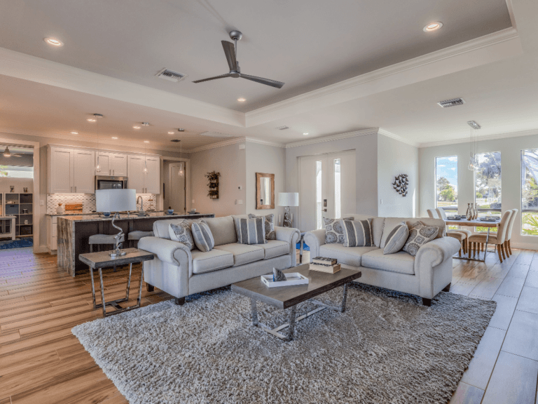 Spacious open-concept living area with two sofas, a rug, coffee table, dining area, and kitchen, featuring large windows and wood flooring—recently updated with flooring repair to address LVP scratches for a flawless finish.